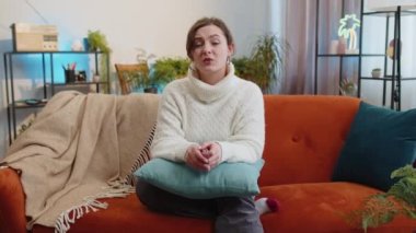 What. Why. Woman raising hands in indignant expression asking reason of failure demonstrating disbelief irritation by troubles at modern home apartment. Portrait of girl in living room sitting on sofa