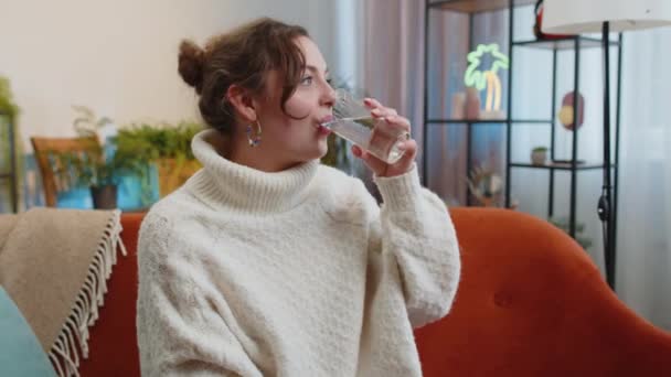 天然のアクアグラスを持っている喉の渇き若い女性は 自宅のリビングルームに脱水症状を防ぐために まだ水を飲んでお尻を作る 良い生活習慣 健康的な痩身 減量の概念を持つ女の子 — ストック動画
