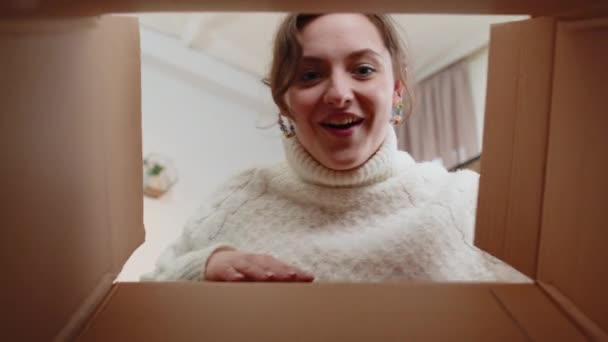 从盒子里往里看年轻快乐的女人在家里打开送货包裹 笑容满面的女购物者 网上商店的顾客打开纸板箱 收到快速邮寄的礼物 — 图库视频影像