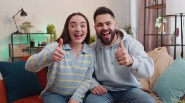 Gibi. Mutlu aile evli erkek kadın kameraya onaylı bir şekilde bakıyor olumlu bir işaret veriyor gibi, olumlu bir şey, evde olumlu geri bildirim gibi. Karı koca oturma odasında kanepede yan yana.