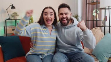 Genç aile evli erkek kadın bağırıyor, başarıyı kutluyor, kazanıyor, vay canına, gol başarısı, iyi haber, piyango ikramiyesi evde. Karı koca birlikte kanepede televizyon izliyorlar.