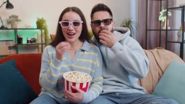 Heyecanlı genç aile evliliği, patlamış mısır yiyen ve ilginç TV dizileri, spor oyunları, filmler, evdeki sosyal medya içerikleri izleyen erkek kadın. Karı koca kanepede yan yana.