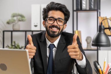 Like. Happy young indian businessman guy working on laptop looking approvingly at camera showing thumbs up, like sign positive something good, positive feedback at office workplace. Freelancer man