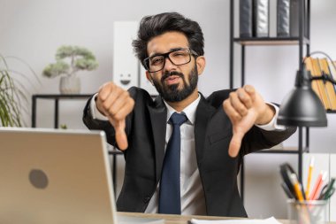 Hoşlanmamak. Merkez ofisteki dizüstü bilgisayarda çalışan üzgün Hintli işadamı hoşnutsuzluğunu, memnuniyetsizliğini ve kötü işini ifade eden işaret hareketini kabul etmiyor. Memnuniyetsizlik ciddi serbest çalışan adam