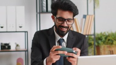 Akıllı telefon ile oynayan Hintli iş adamı heyecan verici mobil uygulama ofis masasında oyun kazanmayı ya da atıcılık oyununu kutluyor. Profesyonel yönetici serbest çalışan adam yeni uygulamanın iyi çalışmalarının tadını çıkarsın.