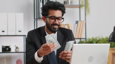Bilgisayarda çalışan zengin Hintli iş adamı nakit para sayıyor, iş yerindeki gelir gelirlerini hesaplıyor. Profesyonel menajer serbest çalışan adam. İş adamları. İstihdam mesleği