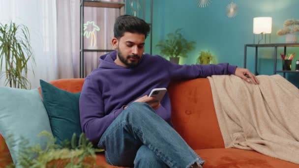 Indian Man Sitting Sofa Uses Mobile Phone Smiles Home Living — Stock Video