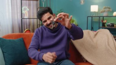 Hintli emlakçı el kaldırıyor. Yeni ev dairesinin anahtarlarını gösteriyor. Ev satın alıyor ya da kiralıyor. Hintli adam kanepede oturuyor.