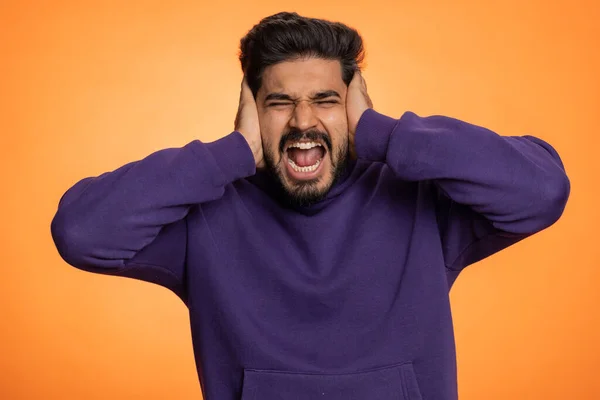 Dont want to hear and listen. Frustrated annoyed irritated indian man covering ears gesturing No, avoiding advice ignoring unpleasant noise loud voices. Handsome hindu guy alone on orange background