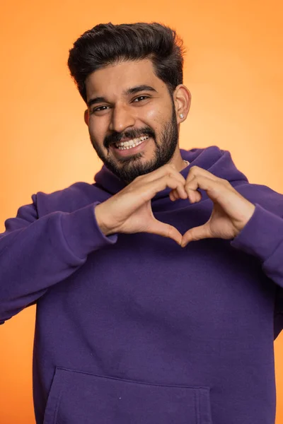 恋爱中的男人25岁的满脸胡须的印地安人做手势表示爱心 表示好感和同情 漂亮的后生小伙子被隔离在橙色工作室的背景下 — 图库照片