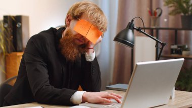 Business people cheating to sleep. Tired inefficient young businessman guy working sleeping on laptop computer with eyes stickers on face at office workplace desk. Bearded lazy manager freelancer man