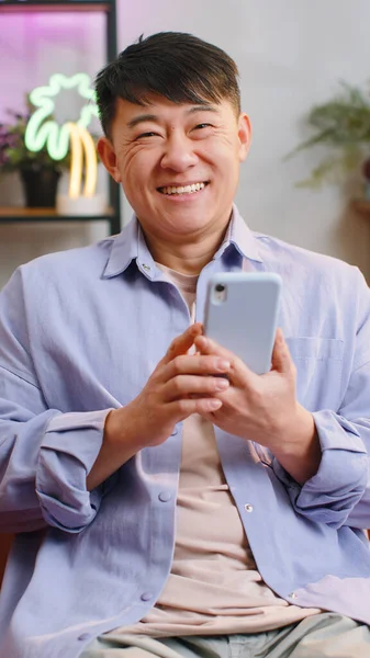 Asian Man Sits Sofa Uses Smartphone Smiles Home Room Apartment — 스톡 사진