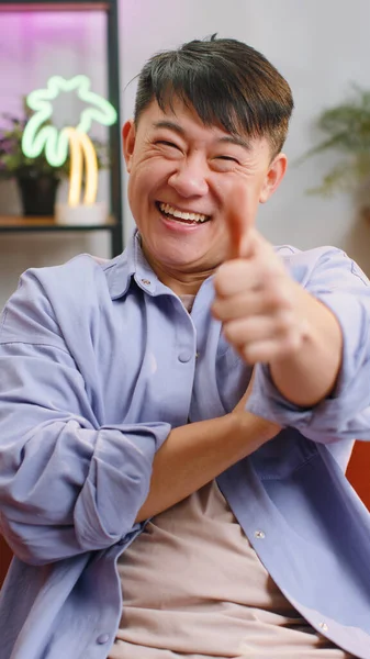 まるで 喜んで興奮したアジア人の男性が承認してカメラを見て親指を表示すると 正の何か 良いニュース 肯定的なフィードバックのような 自宅のリビングルームで大人の中国人男性 — ストック写真