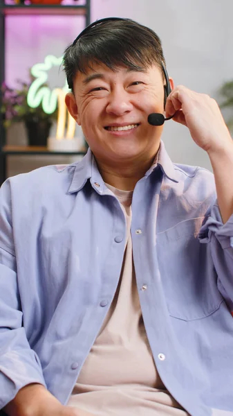 亚洲英俊男子头戴耳机 自由职业工人 呼叫中心或支助服务运营商求助热线 与客户或同事交谈 在家里挥手致意 垂直方向 — 图库照片