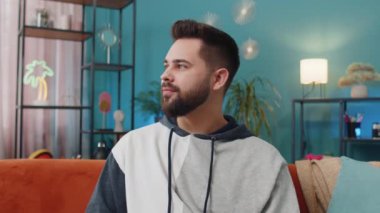 Evdeki koltukta gülümseyen mutlu, sakin beyaz adamın portresi. Dostça gülümseyen, mutlu bir yüz ifadesi. Hayal kurma, rahatlama, tatmin olma konsepti. Genç adam oturma odasında.