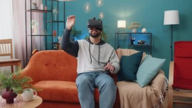 Sanal gerçeklik teknolojisi VR uygulama kulaklığı kullanarak 3D video oyunu simülasyonu izlemek için heyecanlı bir adam. Modern ev dairesindeki kanepede gözlüklü bir adamın portresi.