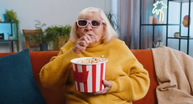 Kanepede 3 boyutlu gözlüklü yaşlı bir kadın patlamış mısır yiyor ve evdeki sosyal medya içeriğinde ilginç bir TV oyunu videosu izliyor. Büyükannem eğleniyor.