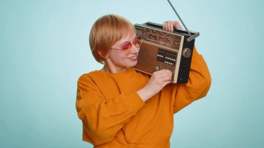 Güneş gözlüklü kadın müzik dinlemek için retro teyp kullanıyor, favori parçaların disko dansını yapıyor, eğleniyor, eğleniyor, klasik teknolojilerin hayranı. Sarışın kız mavi arka planda izole edilmiş.