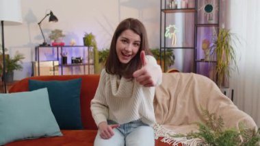 Gibi. Mutlu heyecanlı kadın kameraya onaylayıcı bir şekilde bakıyor, olumlu bir şey gösteriyor, iyi haber, olumlu geri bildirim gibi. Oturma odasındaki kanepede oturan genç kızın portresi.