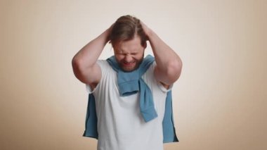 Sakallı beyaz adam umutsuzluk yalnızlık, sinir krizi, mağlubiyet piyango sonuçları, kötü şans kaybı, şanssız haberler karşısında şaşırıyor. Stüdyo bej arka planda izole genç adam