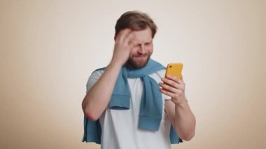 Kafkasyalı adam cep telefonu daktilo kullanıyor. Tarayıcı takibini kaybediyor. Ani piyango sonuçları, kötü şans, kayıp, başarısızlık. Yakışıklı, tek başına bej renkli stüdyo arka planında, kapalı alanda izole edilmiş.
