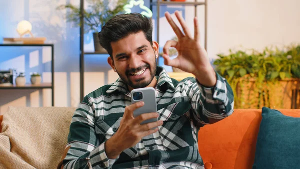 快乐的印地安人用手机打字说 发现大获全胜好消息庆祝彩票中奖做得奖手势 家里的印度教年轻人坐在沙发上 — 图库照片