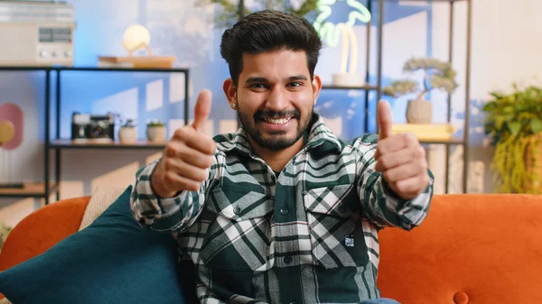 Stock image Like. Happy excited indian man looking approvingly at camera showing thumbs up, like sign positive something, good great news, positive feedback. Young hindu guy sitting on couch at home living room