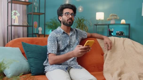 Indian Man Sitting Sofa Uses Mobile Phone Smiles Home Living — 비디오