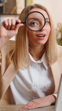 Ofiste çalışan araştırmacı bilim adamı bir iş kadını elinde büyüteçle kameraya bakıyor. Büyütülmüş komik gözüyle analiz yapıyor. Serbest çalışan kadın. Dikey çekim