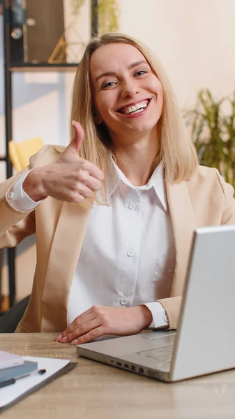 在笔记本电脑上工作的快乐的女商人满意地看着展示大拇指的相机 就像在办公室里签积极正面的东西 积极的反馈 自由职业者的女人 垂直方向 — 图库照片