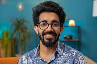 Portrait of happy calm indian man at home couch smiling friendly, glad expression looking away dreaming resting, relaxation feel satisfied concept good news, celebrate win. Hindu guy in living room