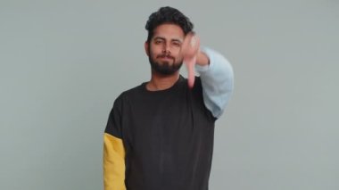 Hoşlanmamak. Hırkalı mutsuz Hintli adam işaret dilini gösteriyor hoşnutsuzluğunu, memnuniyetsizliğini, hoşnutsuzluğunu, hoşnutsuzluğunu ifade ediyor. Yakışıklı bir genç. Gri arka planda çekilen kapalı stüdyo.
