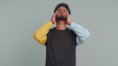 Kazak giyen yakışıklı Hintli sakallı adam baş ağrısı problemini tedavi etmek için tapınakları ovuyor, tansiyon, migain, stres, ekşitme, acı içinde kıvranıyor, yüksek tansiyon gri arka planda tek başına izole edilmiş.