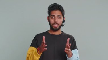 Kulaklık takan gülümseyen Hintli adam, serbest çalışan, çağrı merkezi ya da destek operatörü yardım hattı, müşteri ya da iş arkadaşıyla konuşmak, iletişim desteği. Gri arka planda yakışıklı bir adam.