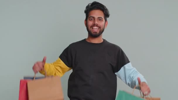 若いインド人男性は 低価格で驚いて見て笑みを浮かべて ブラックフライデーの休日に買い物袋 広告割引を示す Shopaholic Hindu男絶縁上のスタジオグレーの背景 — ストック動画