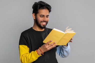 Mutlu Hintli adam komik bir masal kitabı okuyor, boş zaman hobisi, bilgelik, eğitim, öğrenme, çalışma, vay be. Yakışıklı Hintli adam gri stüdyo arka planında tek başına.