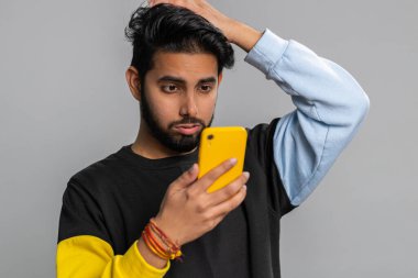 Hintli adam cep telefonu daktilosu kullanıyor. Ani piyango sonuçlarını kaybediyor. Kötü talih, kayıp, başarısızlık. Yakışıklı Hintli adam, gri stüdyo arka planında tek başına, kapalı alanda.