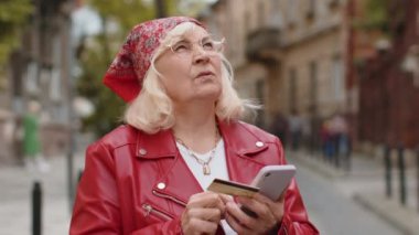 Üst düzey bir kadın kredi kartı akıllı telefonu kullanıyor. Parayı transfer ederken, online alışveriş yaparken, yemek siparişi verirken, otel odasında rezervasyon yaparken. Şehir caddesinde yürüyen yaşlı bir büyükanne.