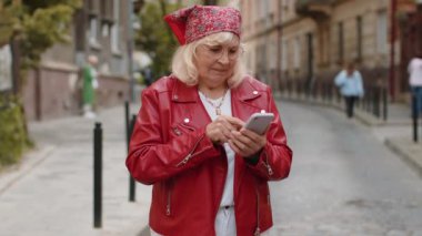 Akıllı telefon kullanarak gülümseyen, mesajlar yazan interneti gezen, işi bitiren, kameraya bakan. Şehir sokaklarında yürüyen yaşlı bir büyükanne. Şehir yaşam tarzları açık havada