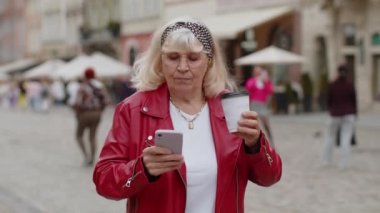 Üst düzey kadın akıllı telefon kullanıyor, ekrana bakıyor, sohbet ediyor, sabah kahvesinin tadını çıkarıyor. Şehir merkezindeki caddede yürüyen yaşlı bir büyükanne, gitmek için kahve içiyor. Kasaba yaşam tarzları