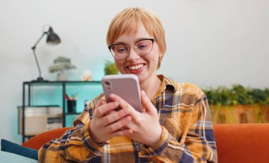 Aman Tanrım. Vay canına. Heyecanlı mutlu, neşeli genç kadın akıllı telefon daktilo kullanıyor. Kazanan kazanır. Zaferi kutlar. Cep telefonlu bir kız, evinde, odasında, kanepede oturuyor.