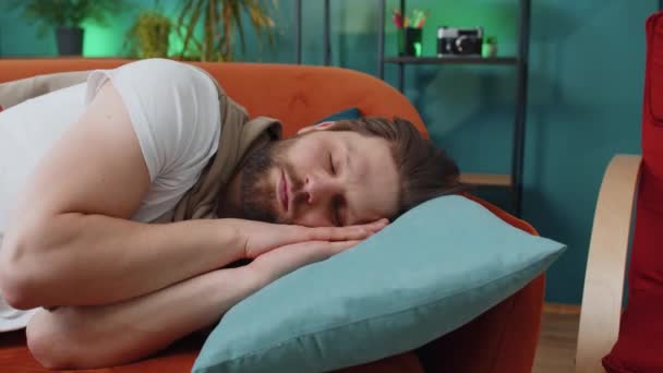 疲倦的年轻人躺在床上 在家里的公寓房间里休息 无忧无虑的白人小伙打盹 睡在舒适的橙色沙发上 枕着枕头 闭上他的眼睛独自享受白天的小睡 — 图库视频影像
