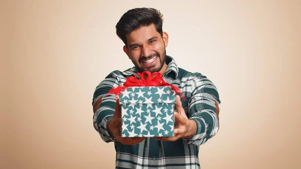 积极向上的笑着的印度年轻人献上生日礼物盒 伸出手来 提供包装好的职业奖金 庆祝派对 胡子后面的家伙孤立在米色工作室的背景 — 图库照片