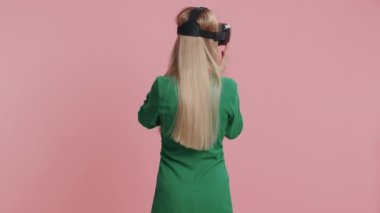 Gerçekçi simülasyon oyunları oynamak için kulaklık uygulaması kullanan genç bir kadın. Sanal gerçeklik 3D 360 videosu izliyoruz. Sanal gerçeklik gözlüklü genç kız aygıtı pembe arka planda, kapalı alanda izole edilmiş.