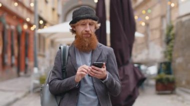 Akıllı telefon kullanan genç adam, harita üzerinde bir rota arıyor mobil navigatör uygulamasında mesaj yazıyor internete takılıyor, işi bitiriyor. Şehir caddesinde yürüyen bir adam. Şehir dışında.