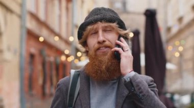 Mutlu sakallı adam uzaktan iletişim kurarak akıllı telefondan konuşuyor. Yakışıklı, genç, yetişkin bir adam telefonda konuşuyor. Şehir caddesinde beklenmedik dedikodular dolaşıyor. Şehir yaşam tarzları açık havada