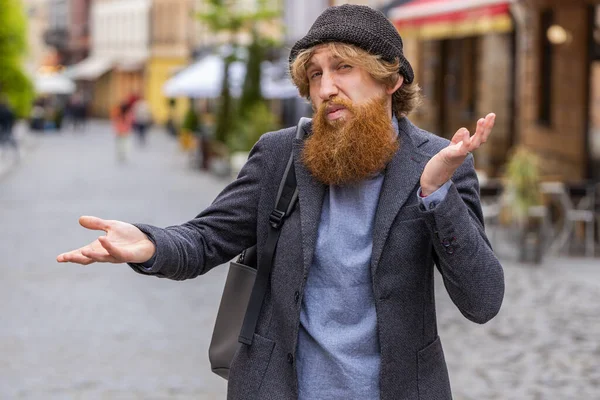 I dont know what to say. Confused young bearded man feeling embarrassed about ambiguous question, having doubts, no idea, being clueless uncertain. Redhead guy walking in urban city street outdoors
