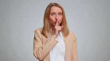 Shh be quiet please, keep my secret. Portrait of young businesswoman presses index finger to lips makes silence gesture sign do not tell anything. Female girl in suit. Pretty woman on gray background