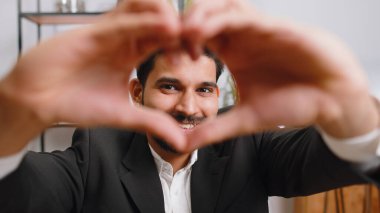 I love you. Indian business man makes symbol of love, showing heart sign to camera, express romantic feelings, express sincere positive feelings at home office workplace. Charity, gratitude, donation