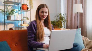 Woman freelancer opens laptop, starts working education on notebook, sends messages, makes online purchases, watching movies at home living room apartment. Portrait of girl sitting on couch. Lifestyle